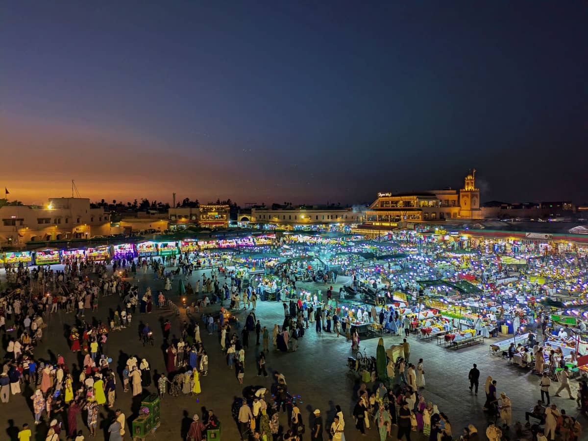 ภาพจัตุรัส Jemaa el-Fnaa ในมาราเกชช่วงรอมฎอนยามค่ำ เต็มไปด้วยผู้คนและแผงอาหารครึกครื้น ใต้ท้องฟ้าโพล้เพล้สีน้ำเงินเข้ม