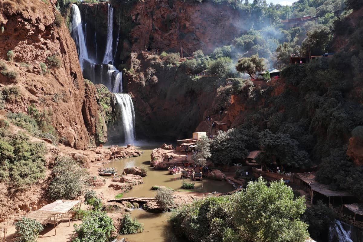 วิวอันตระการตาของน้ำตก Ouzoud ใกล้เมือง Marrakech ในฤดูใบไม้ผลิ พร้อมน้ำตกไหลเป็นชั้น ต้นไม้เขียวขจี และระเบียงริมแม่น้ำขนาดเล็ก