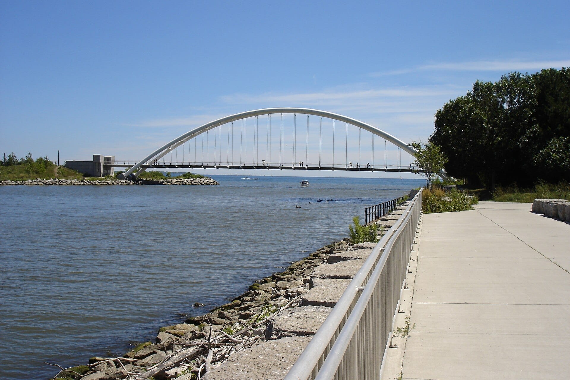 Martin Goodman Trail ทอดยาวตามเส้นทางลาดยางริมทะเลสาบ Ontario โดยมี Humber Bay Arch Bridge สีขาวพาดข้ามผืนน้ำสีฟ้าที่สงบนิ่งภายใต้ท้องฟ้าแจ่มใส