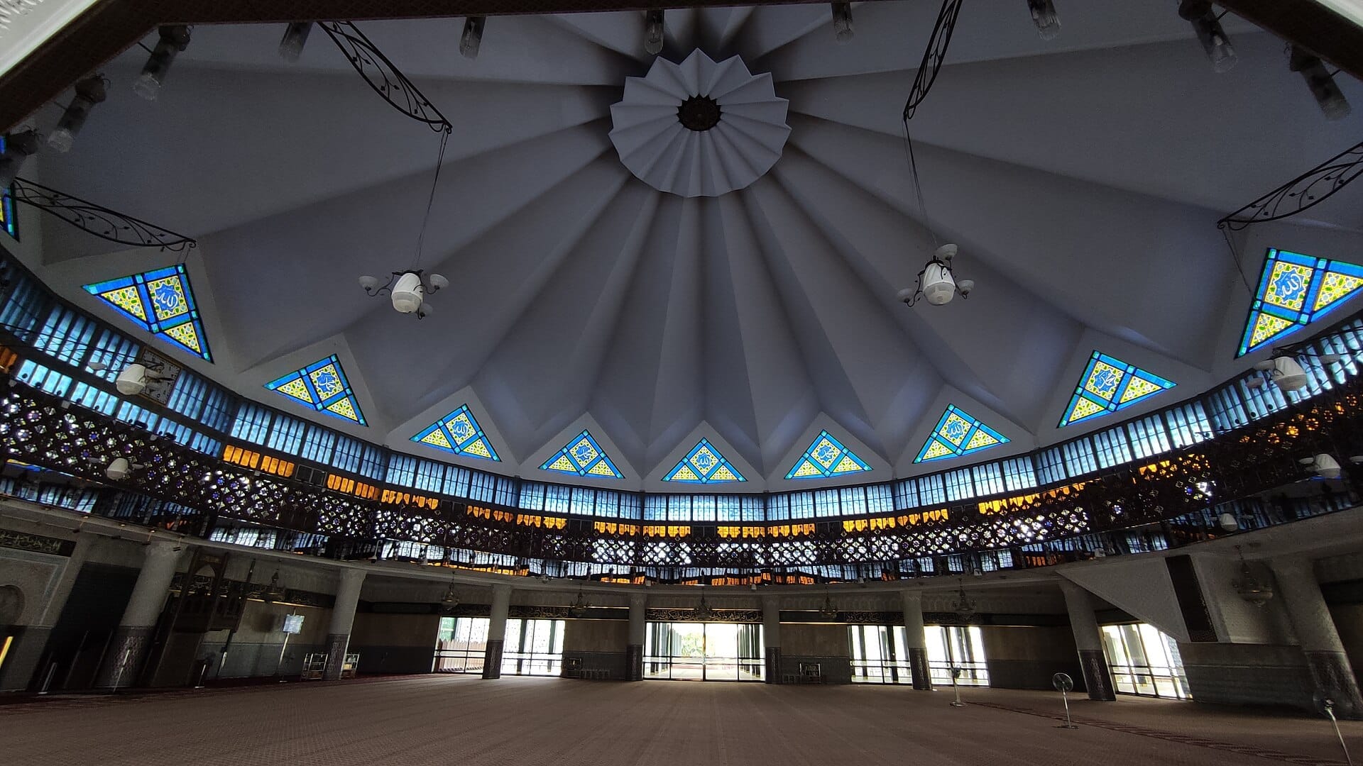 Interior view of Masjid Negara, featuring its striking modernist dome, geometric stained glass windows, and open prayer hall illuminated by natural light.