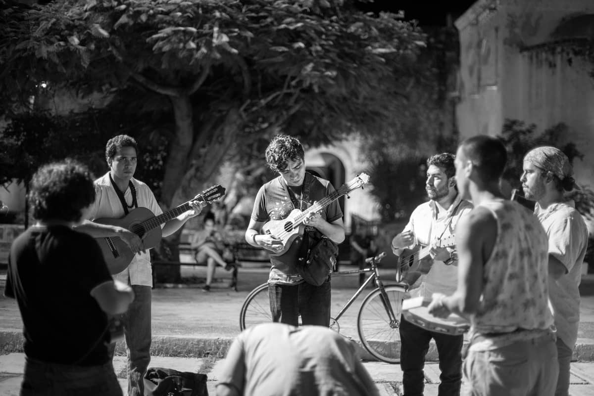 Eine Gruppe Straßenmusiker, die nachts gemeinsam Gitarre spielen und singen in einem lebhaften öffentlichen Außenbereich.