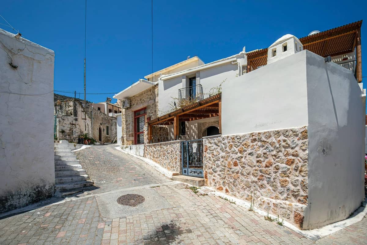Kleine Wohnstraße auf Kreta mit steinernen Häusern und Balkonen unter einem klaren blauen Himmel.