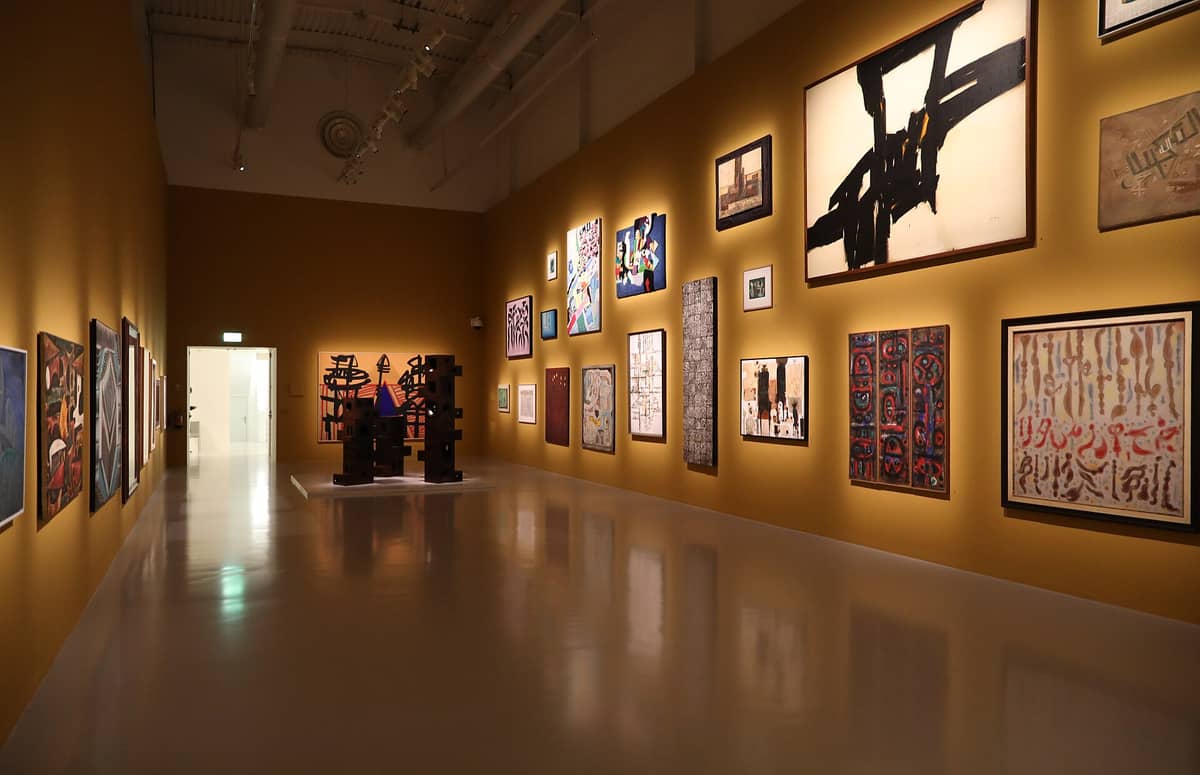 Innenansicht einer Galerie im Mathaf: Arabisches Museum für moderne Kunst, mit Wänden voller moderner arabischer Gemälde und Skulpturen, warm beleuchtet, keine Menschen zu sehen.