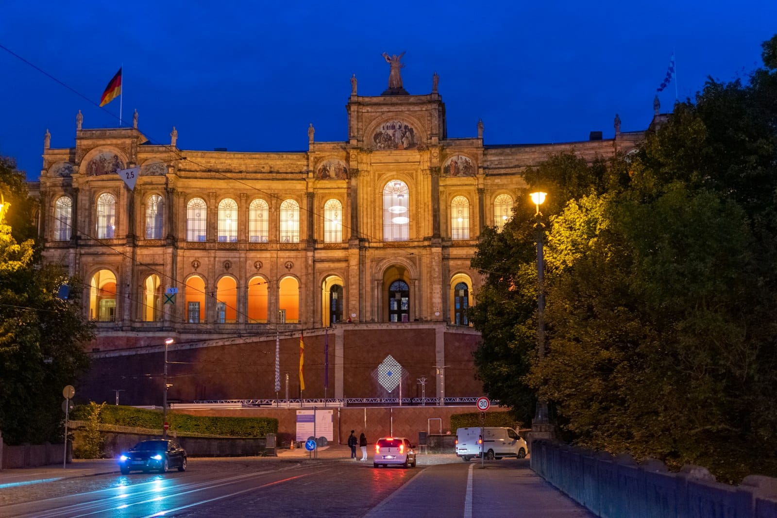 Maximilianeum ในมิวนิกยามค่ำ ส่องแสงสีทองเห็นหน้าตานีโอกอธิคและรูปปั้น เด่นจากปลายถนน Maximilianstraße