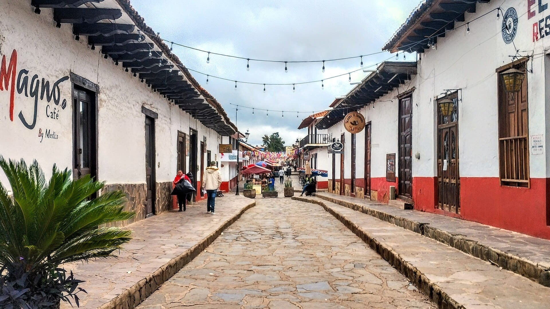 Via principale di Mazamitla con pavimentazione in ciottoli, edifici coloniali bianchi e rossi, luci a festoni e alcune persone che camminano in una giornata nuvolosa.