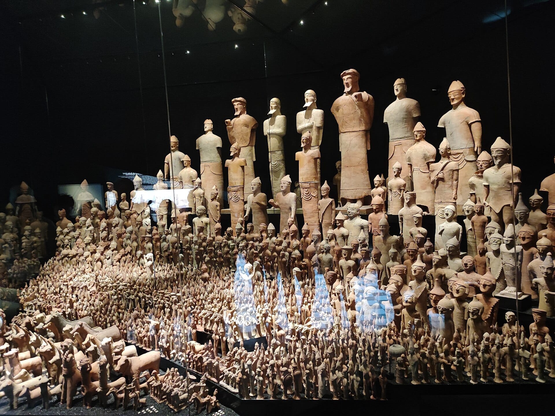 รูปปั้นเทอร์ราคอตตาโบราณหลายร้อยชิ้นจาก Museum of Mediterranean and Near Eastern Antiquities ที่จัดแสดงในตู้กระจกภายใต้แสงไฟอ่อนนุ่มและดราม่า