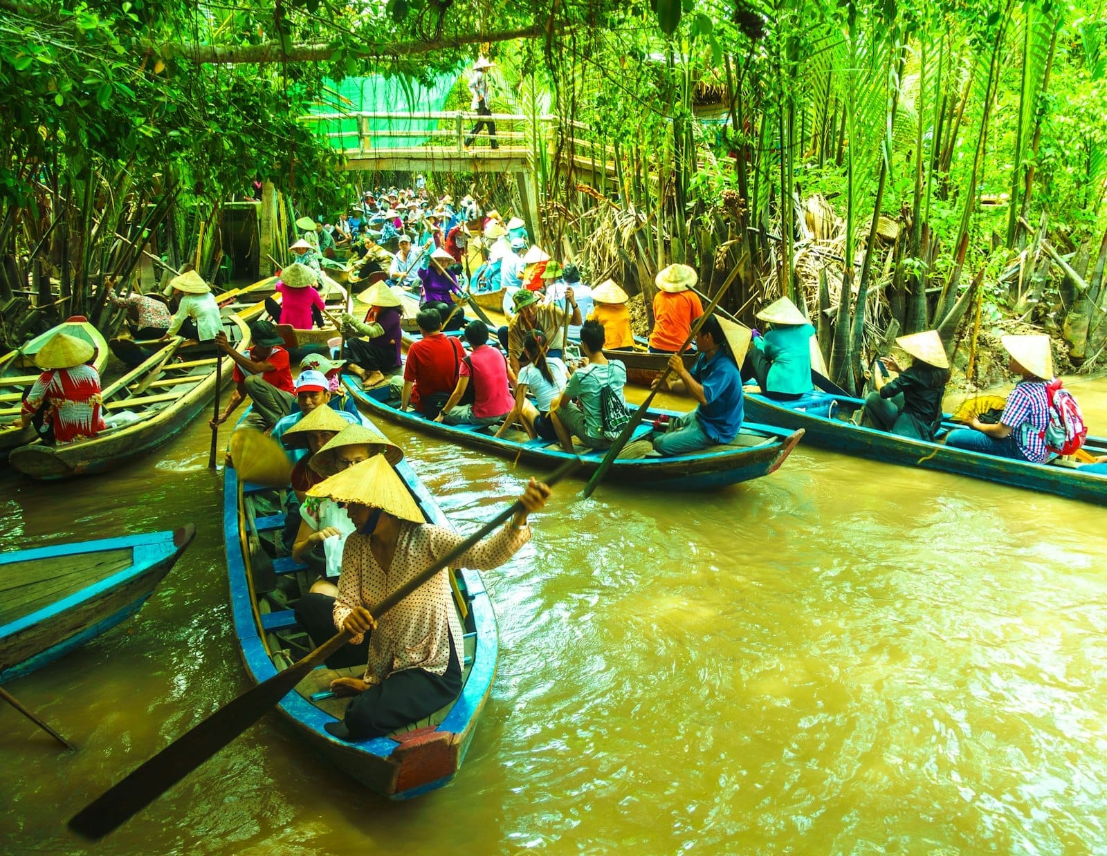 Botes de madera tradicionales con personas con sombreros cónicos navegan por exuberantes canales verdes en el vibrante Delta del Mekong.