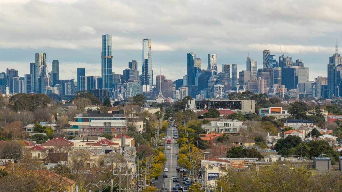 Ein weiter Blick auf die Vorstadtstraßen von Melbourne, die sich unter einem bewölkten Himmel zur modernen Skyline der Stadt erstrecken.