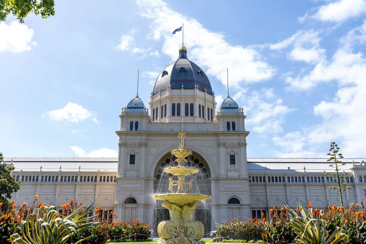 Vista frontale del Royal Exhibition Building di Melbourne, una grandiosa struttura dell'era vittoriana con cupola e colonne classiche, alla luce del giorno con giardini e una fontana.
