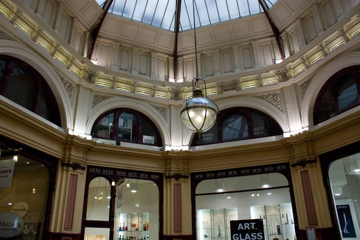 Vista interna del Block Arcade di Melbourne con ornamentali archi vittoriani, tetto a lucernario, grande lampada a sospensione e negozi con vetrine in vetro.