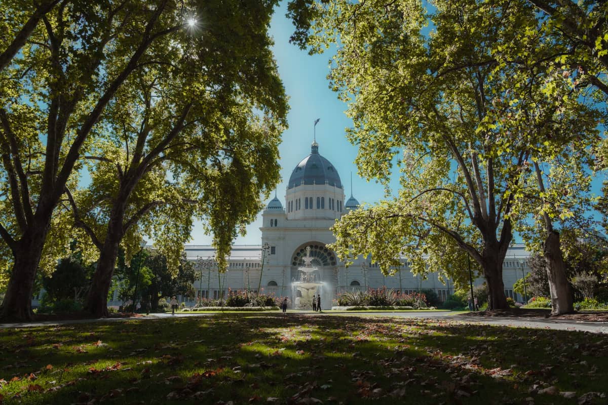 Ampio paesaggio del Royal Exhibition Building di Melbourne incorniciato da lussureggianti alberi verdi, con una cupola centrale che si innalza dietro una fontana d'acqua nei Carlton Gardens.