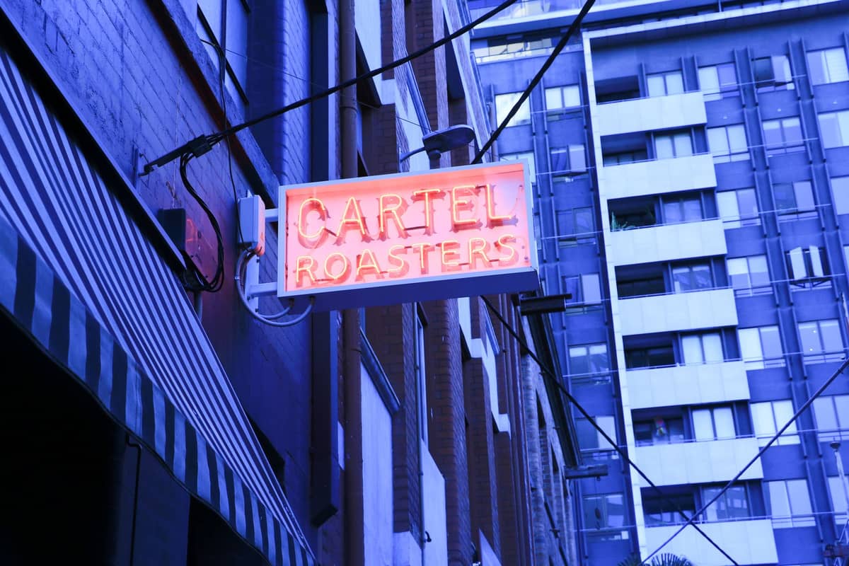 Leuchtreklame mit der Aufschrift 'Cartel Roasters' über einer Straße in Melbourne, im Hintergrund sind Stadtgebäude zu sehen.
