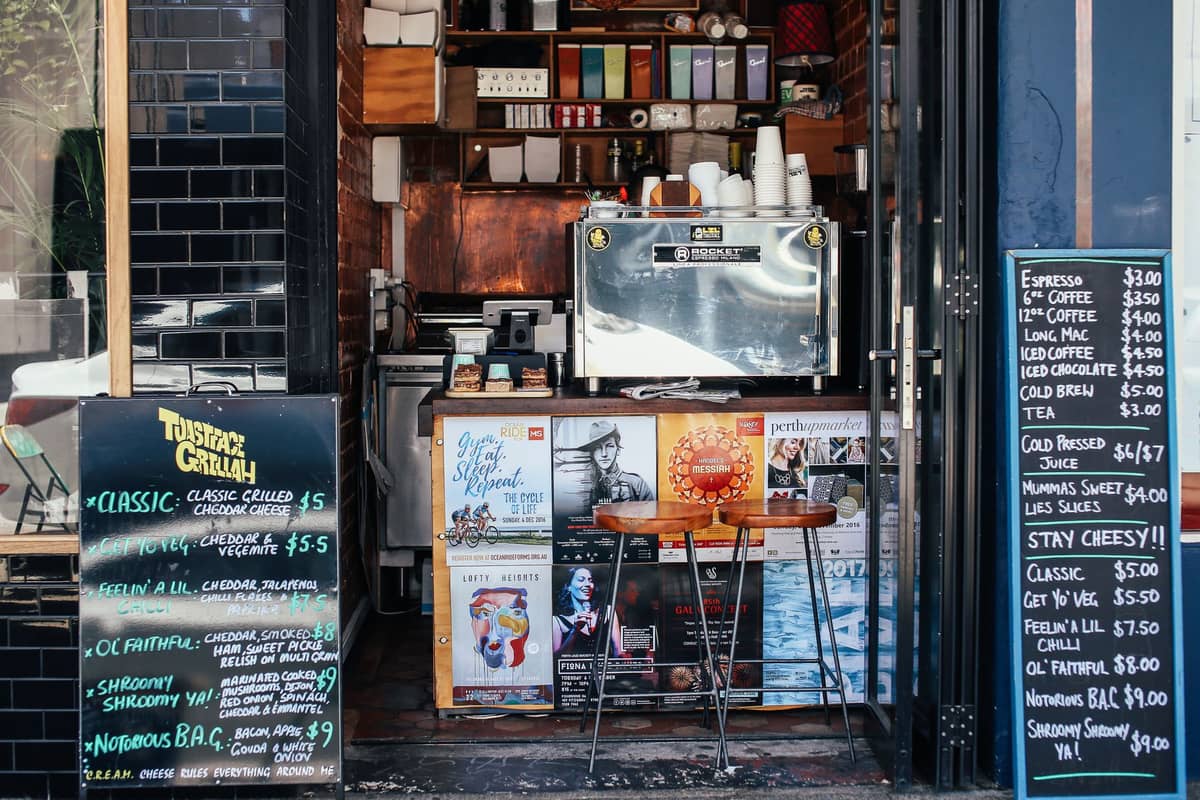 Kleines Café-Ladenfront in Melbourne mit Espressomaschine, Hockern, handgeschriebenen Menütafeln und Flyern, die die unabhängige Kaffeekultur der Stadt widerspiegeln.