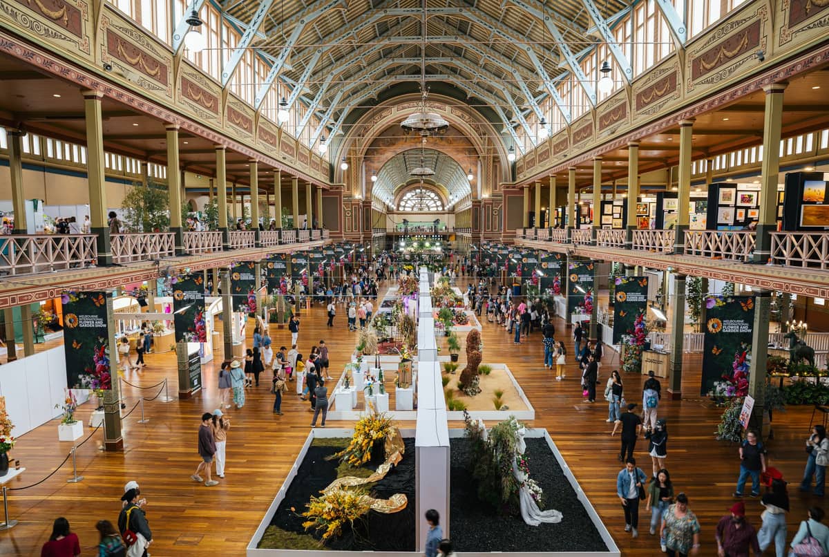 Gran multitud explorando coloridas instalaciones florales y puestos de vendedores en el Royal Exhibition Building de Melbourne durante un importante festival.
