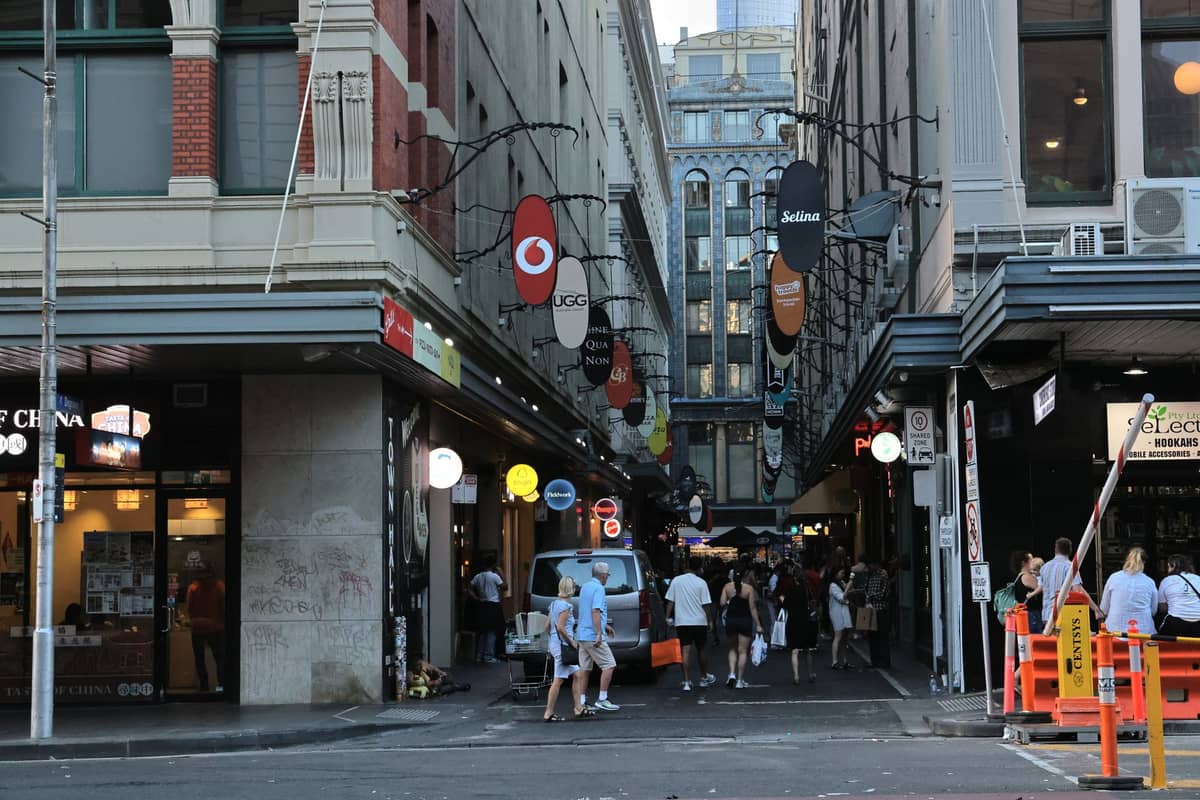 Pedestrian laneway in central Melbourne with people walking between shops, featuring typical signage and Victorian era architecture.