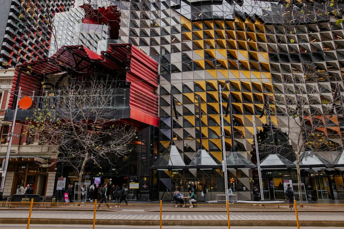 Beeindruckende zeitgenössische Fassade des Design Hub der RMIT University mit geometrischen Paneelen, Menschen auf der Straße, ein großartiges Beispiel für Melbournes eigenwillige Kunst- und Kulturszene.