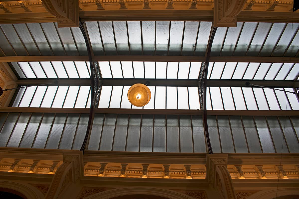 Gewölbte Decke aus Glas und Eisen einer historischen Passage, mit verzierten Details und warmem Licht, wahrscheinlich Melbournes Block Arcade oder Royal Arcade.