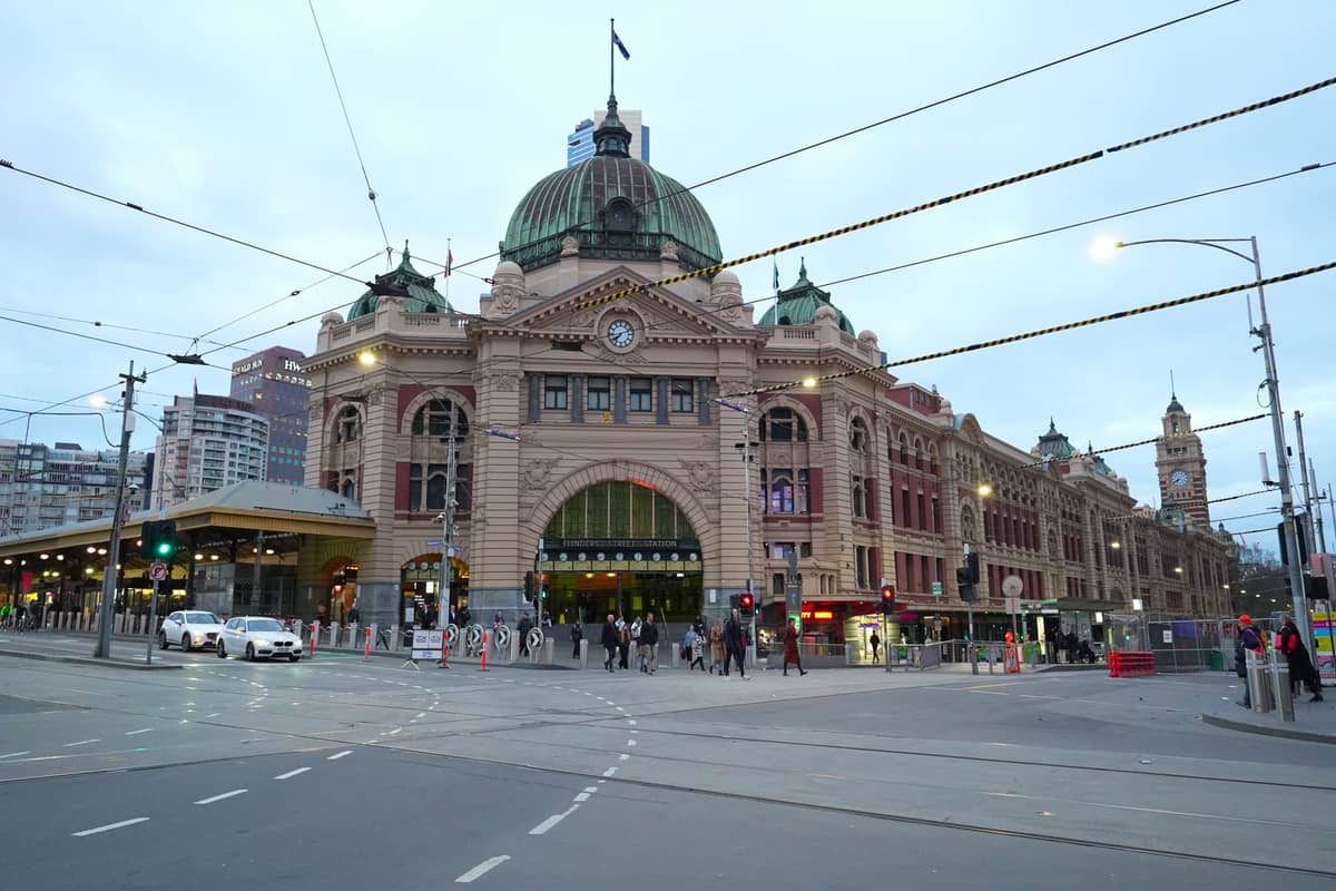 Vista ampia della Flinders Street Station nel centro di Melbourne al crepuscolo con linee del tram e pedoni presenti.