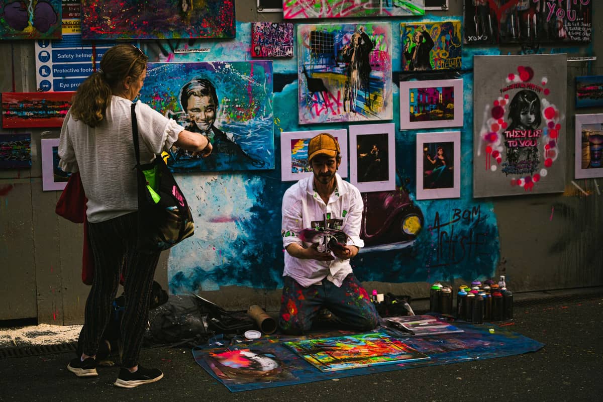 Ein Straßenkünstler, der bunte Gemälde direkt in einer Gasse in Melbourne verkauft, während ein Kunde die lebhafte Kunstausstellung durchstöbert.