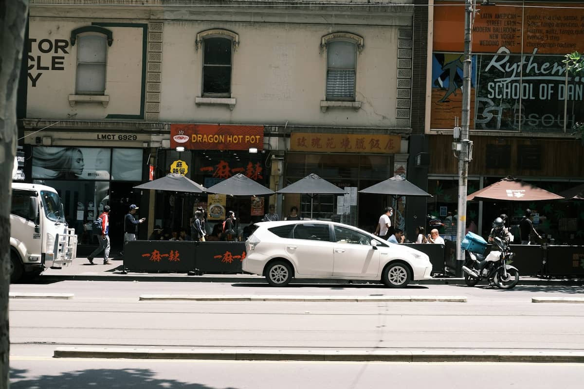 Straßenansicht mit Menschen, die draußen im Dragon Hot Pot und anderen asiatischen Restaurants im multikulturellen Viertel von Melbourne speisen.