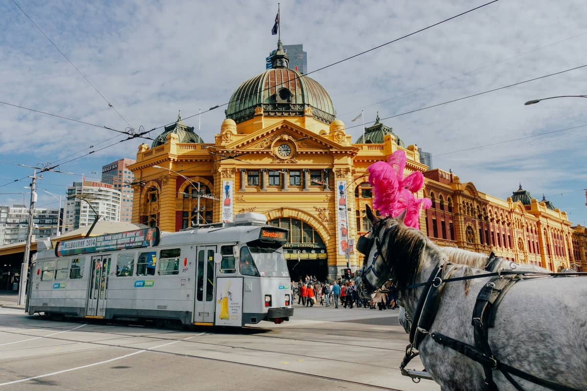 La histórica Estación de Flinders Street en Melbourne con un tranvía tradicional pasando y un carruaje tirado por caballos en primer plano.