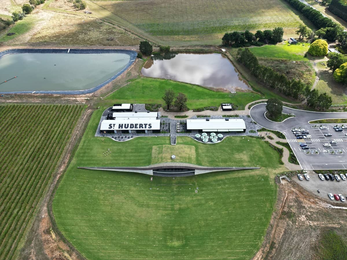 Luftaufnahme des Weinguts St Hubert's im Yarra Valley mit Weinbergen, modernen Gebäuden, Parkplatz und Seen.