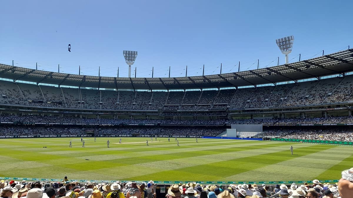 Panoramablick in das Melbourne Cricket Ground während eines Live-Cricket-Spiels, mit einer großen Menschenmenge im Stadion und Spielern auf dem Spielfeld.