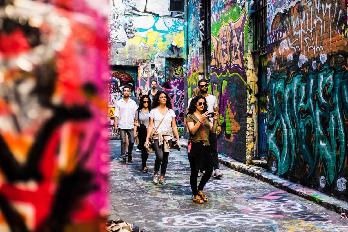 Grupo de personas caminando por un callejón de Melbourne cubierto de coloridos murales y graffitis en las paredes y el suelo.
