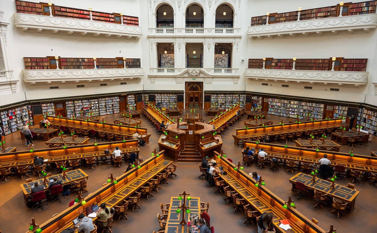 Innenansicht des La Trobe Reading Room in der State Library Victoria mit Menschen, die an langen Holztischen unter einer Kuppeldecke lernen.