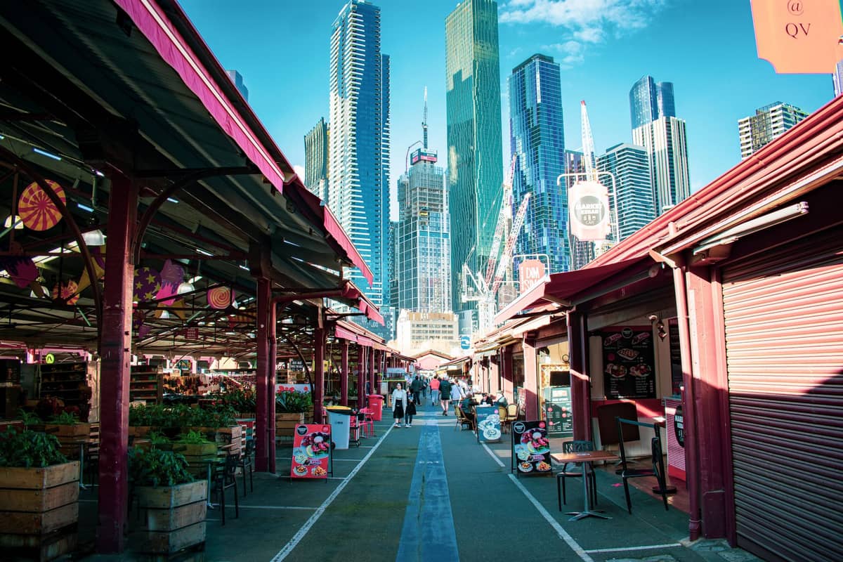 Freiluftmarktstände am Queen Victoria Market mit Passanten und den Wolkenkratzern von Melbourne im Hintergrund