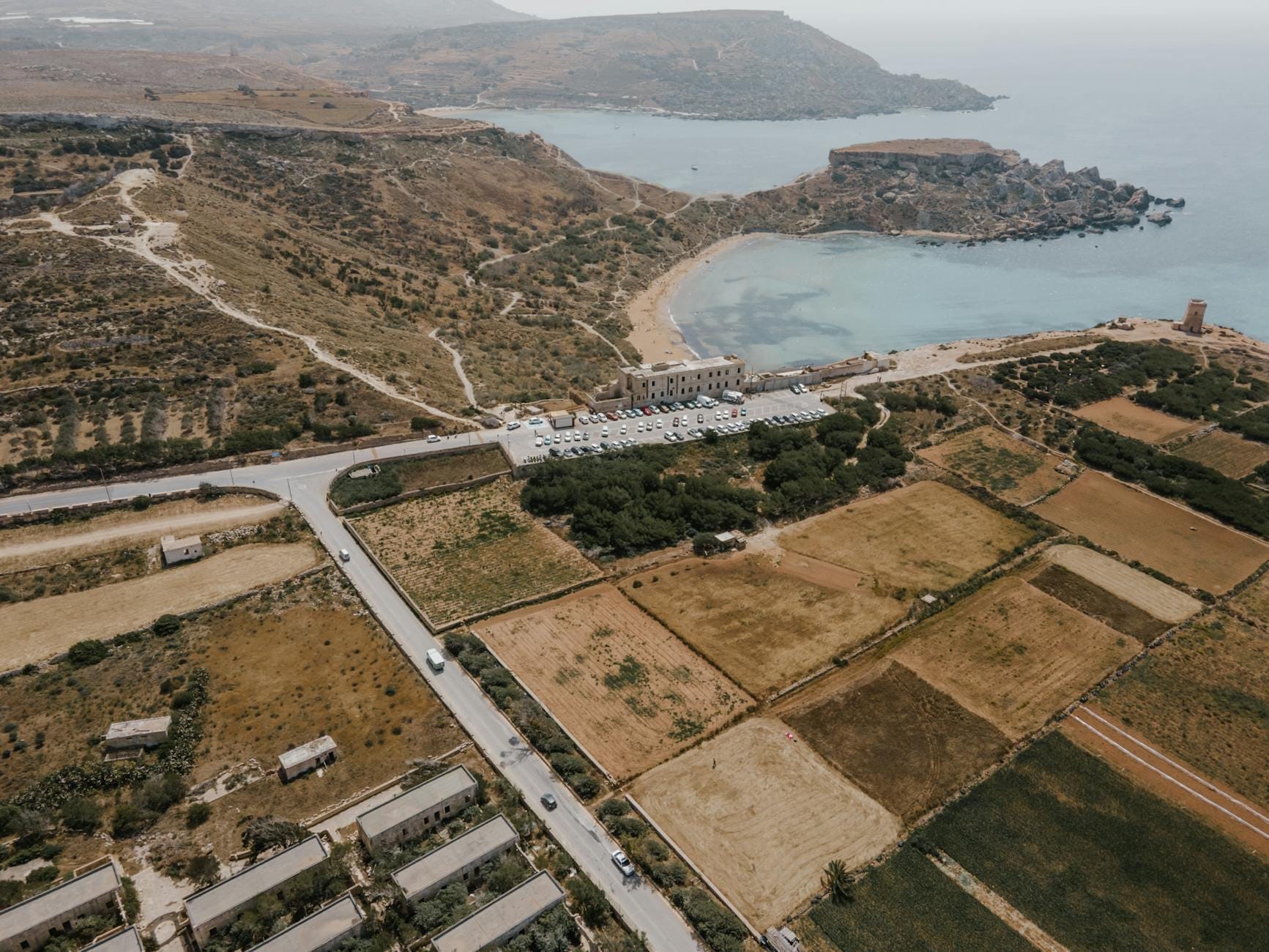 Vista aerea di Mellieħa Bay con una lunga spiaggia sabbiosa, acque calme e azzurre, la vicina riserva naturale e i campi agricoli lungo la costa maltese.