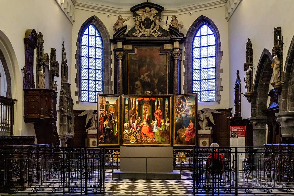 Interior view of Memling in Sint-Jan museum, showing stained glass windows, sculptures, and a Hans Memling altarpiece in a medieval hospital chapel.
