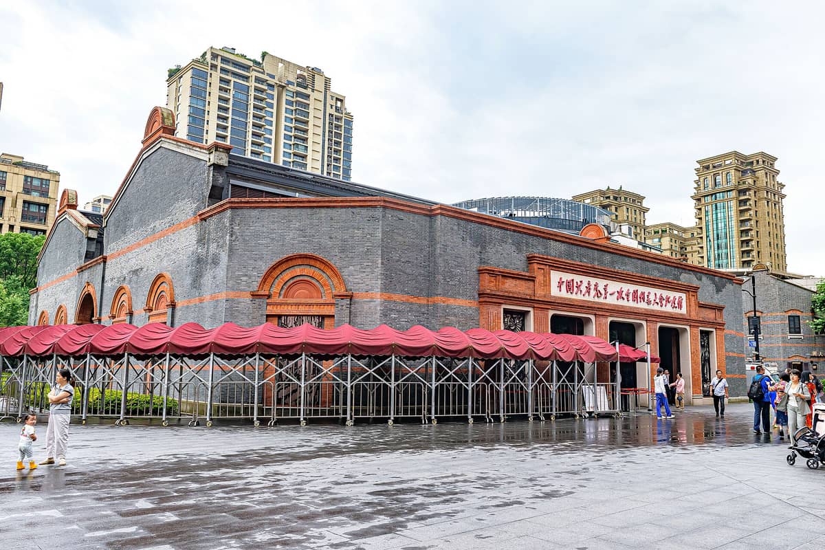 Die Außenfassade der Gedenkstätte des Ersten KPCh-Nationalkongresses: ein erhaltenes Shikumen-Gebäude mit roten Ziegelakzenten und Besuchern davor, Shanghai.