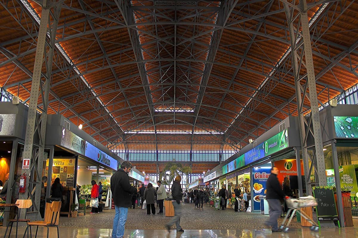 มุมมองภายในแบบกว้างของ Mercado Agrícola de Montevideo พร้อมหลังคาเหล็กและกระจก ร้านค้าในตลาดสมัยใหม่ และนักช้อปที่เดินผ่านโถงกว้างขวาง