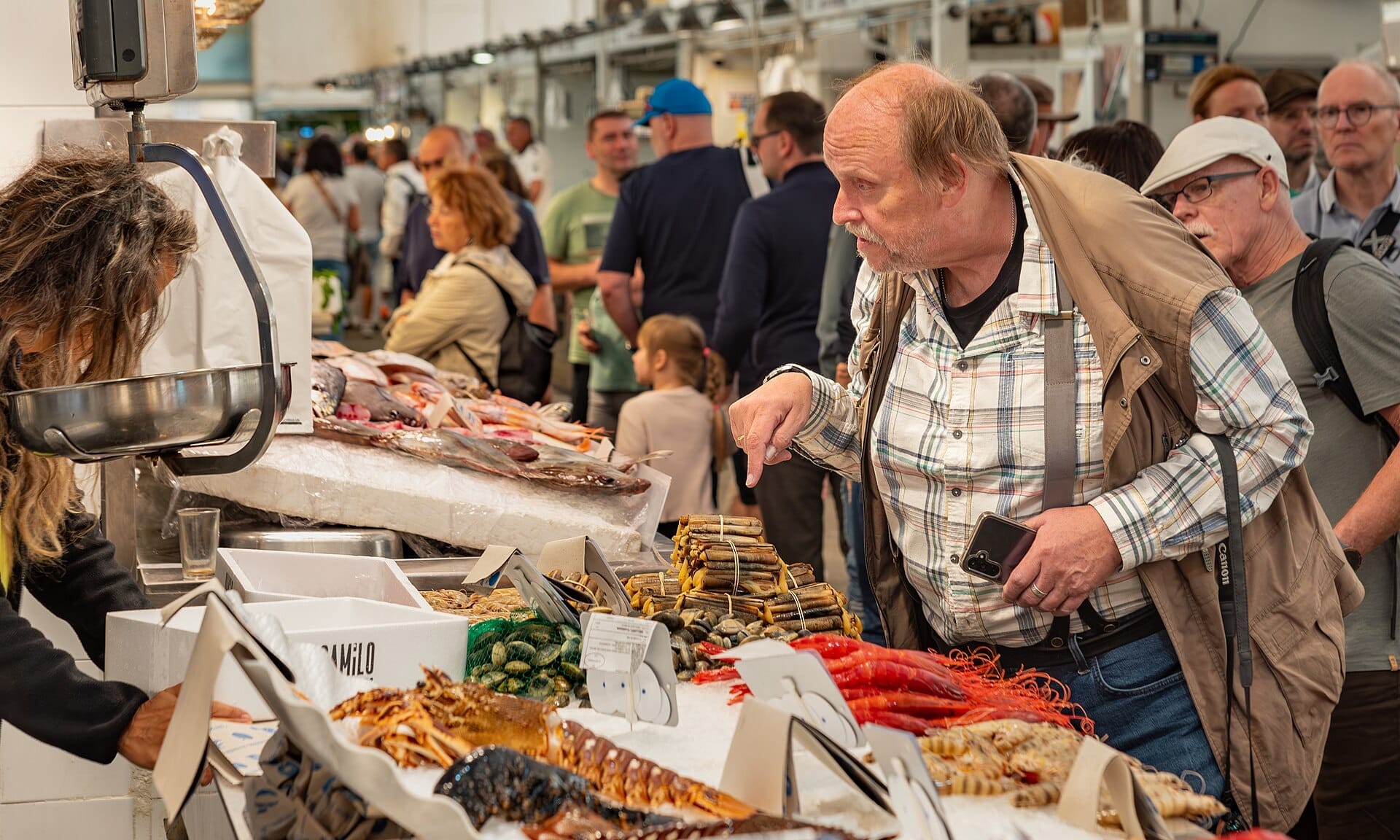 Vivace banco del pesce al Mercado Central de Abastos di Cádiz, con persone che osservano pesce fresco, frutti di mare e prelibatezze locali sotto le luci brillanti del mercato.