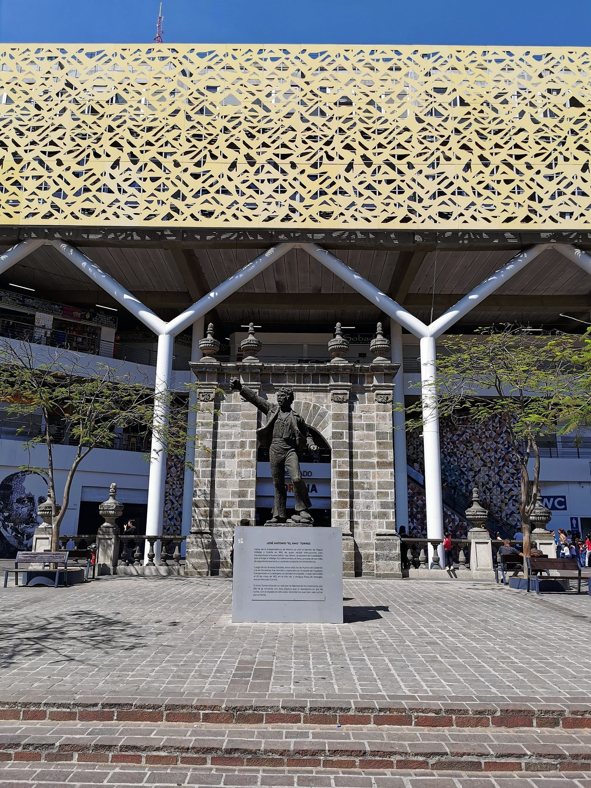 Vista frontale del Mercado Corona a Guadalajara, con la sua facciata moderna, la statua centrale e la piazza esterna in una giornata limpida e soleggiata.