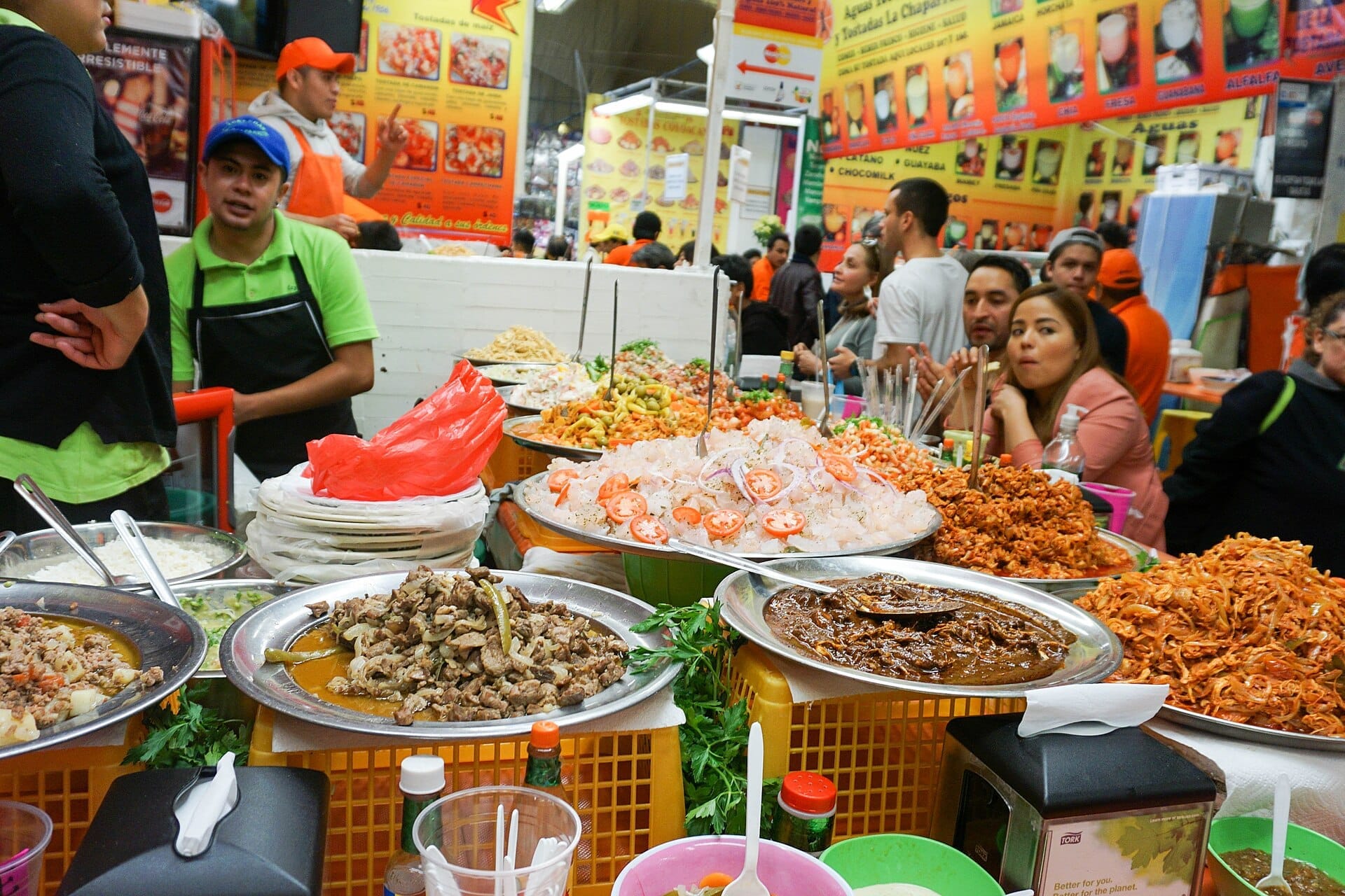 Vivace bancarella di cibo al Mercado de Coyoacán con piatti colorati, personale in grembiule e folle animate che gustano la cucina tradizionale messicana.