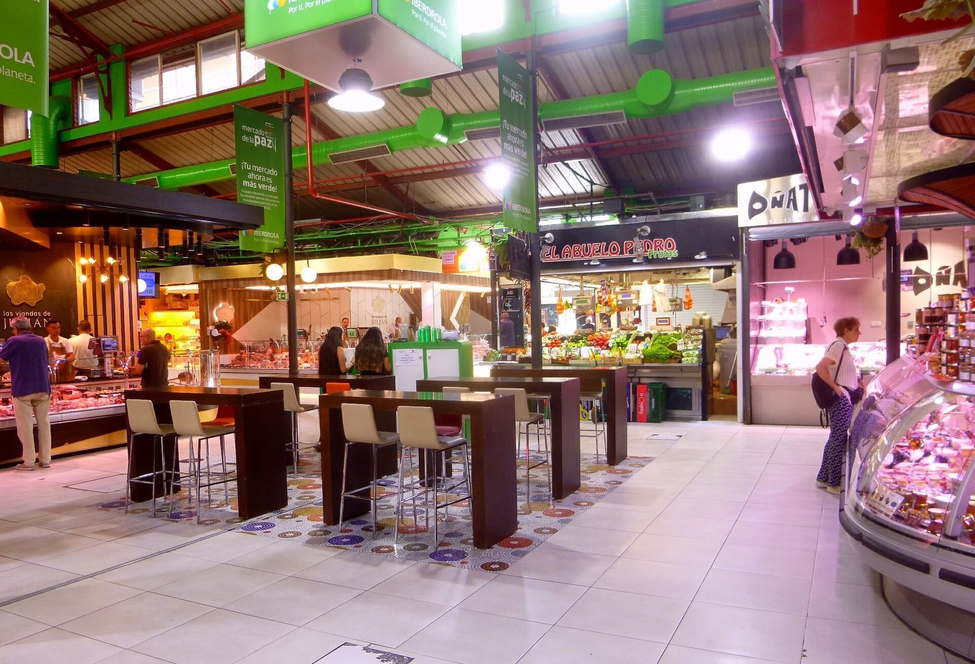 Interno luminoso del Mercado de La Paz con bancarelle di cibo, prodotti colorati e persone che fanno shopping e cenano a tavoli moderni.