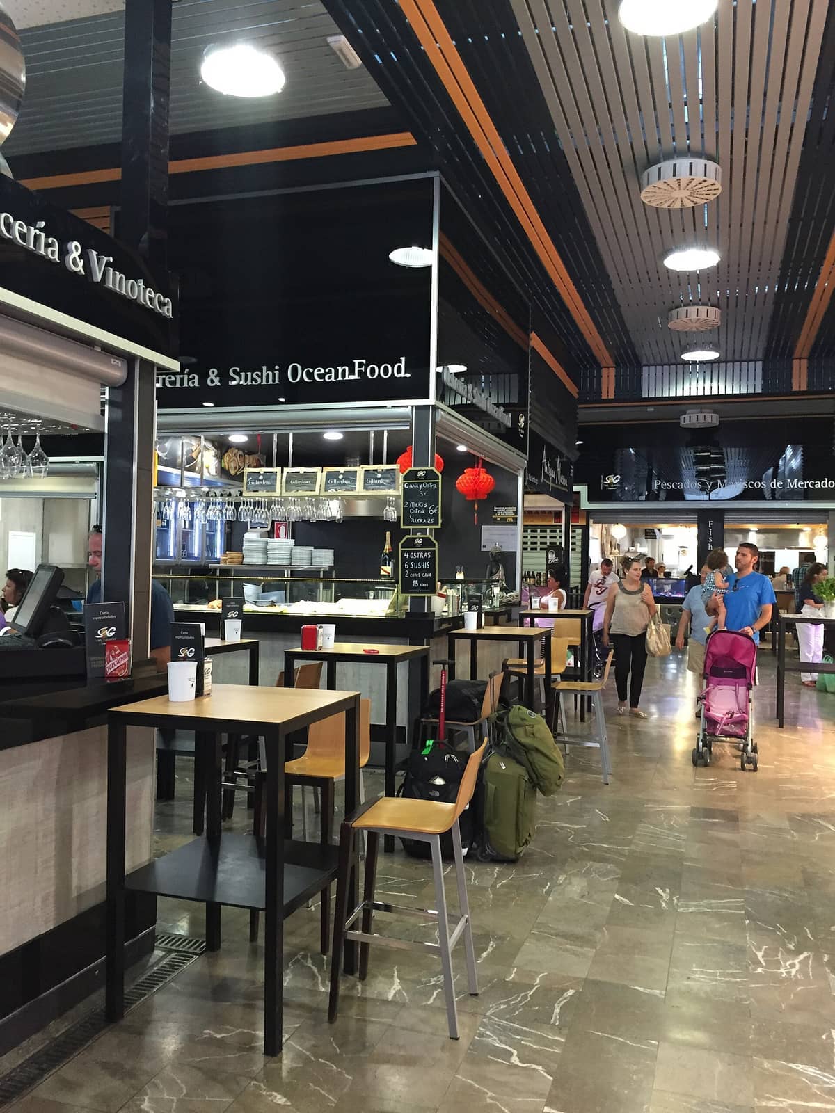 มุมมองภายในของ Mercado de San Agustín ในเมือง Granada มีแผงขายอาหารสมัยใหม่ โต๊ะสูง และนักช้อปที่เดินเที่ยวชมตลาดอันสว่างไสว