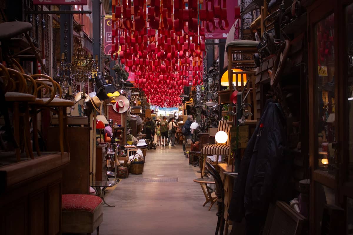 วิวภายใน Mercado de San Telmo เห็นแผงขายของเก่า ของตกแต่งหลากหลายกับผู้คนใต้หลังคาตกแต่งโคมไฟสีแดง