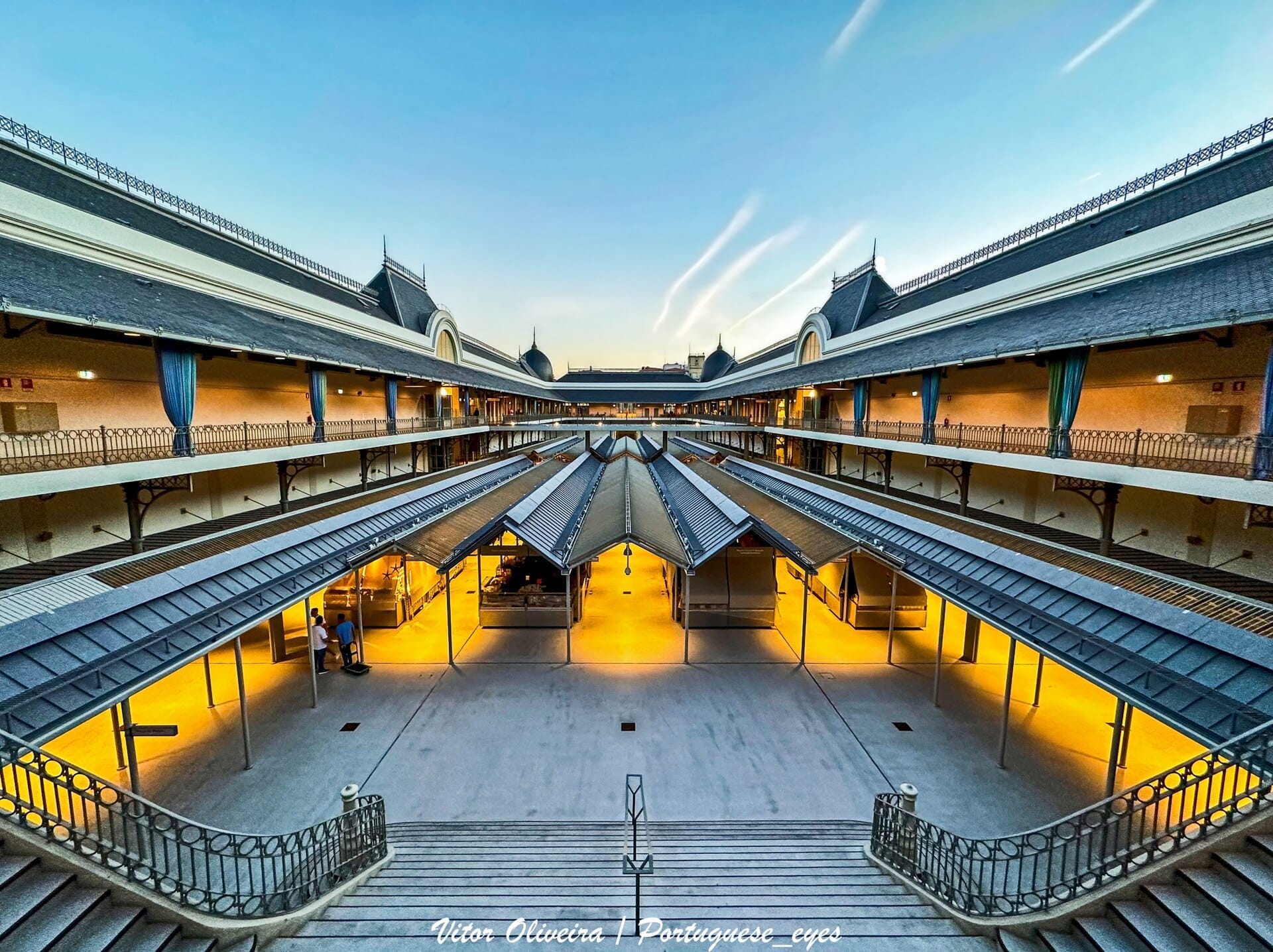 La restaurata sala mercato a due piani del Mercado do Bolhão, bancarelle vuote che brillano sotto archi in ferro al tramonto, catturata dalla grande scalinata centrale.