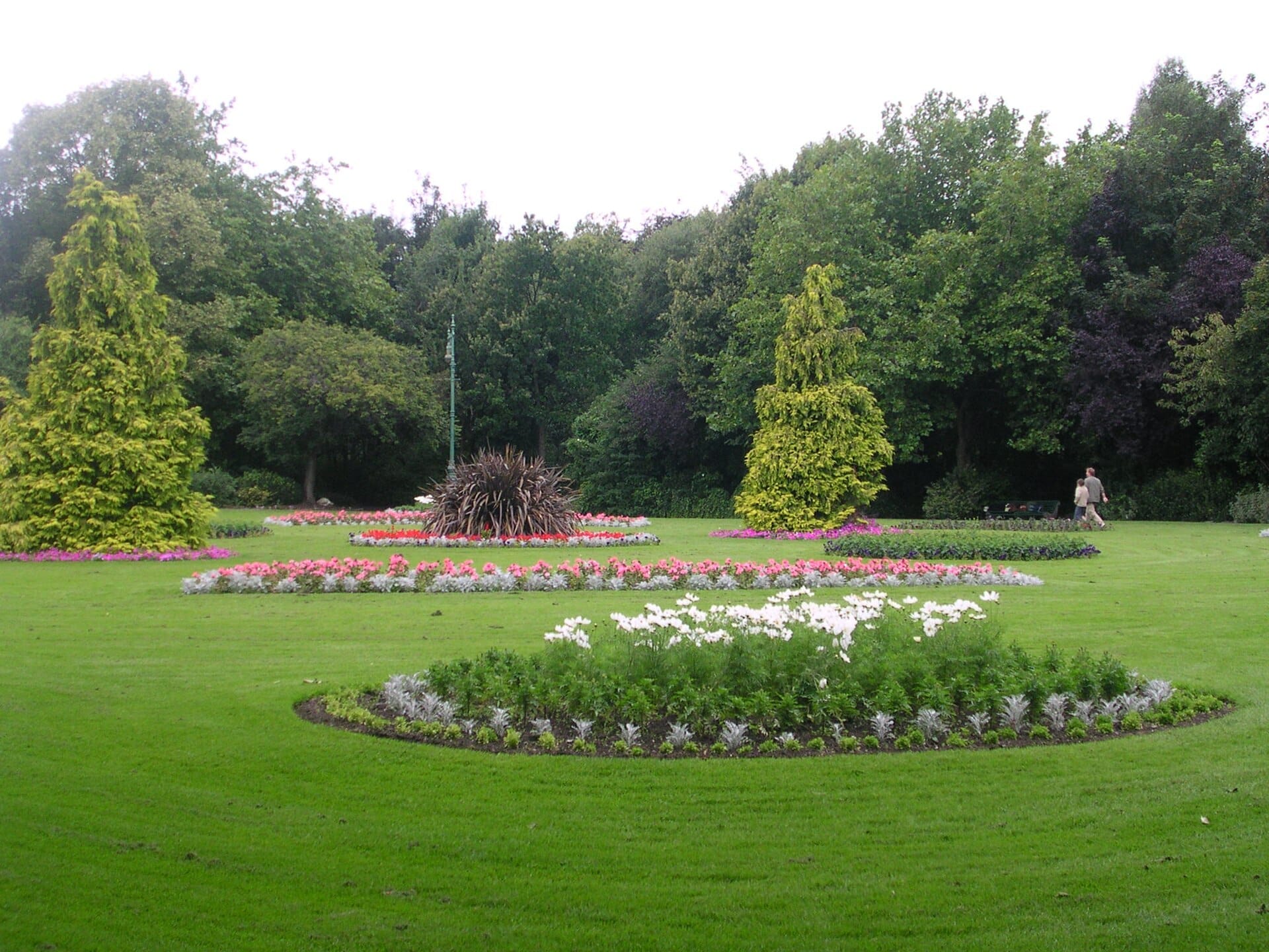 Aiuole curate e lussureggianti prati verdi a Merrion Square Park, con alberi alti e una persona che cammina sullo sfondo.