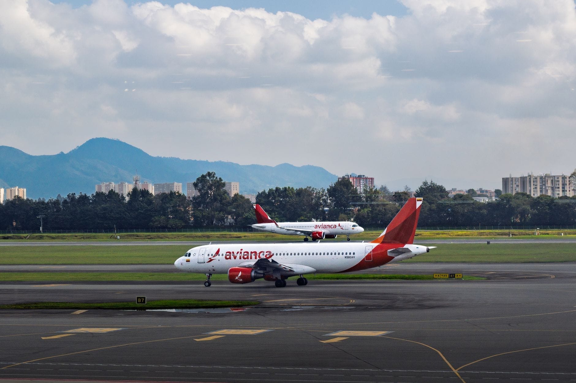 Dois aviões da Avianca no pátio com o skyline e as montanhas da Cidade do México ao fundo, vistos do aeroporto.