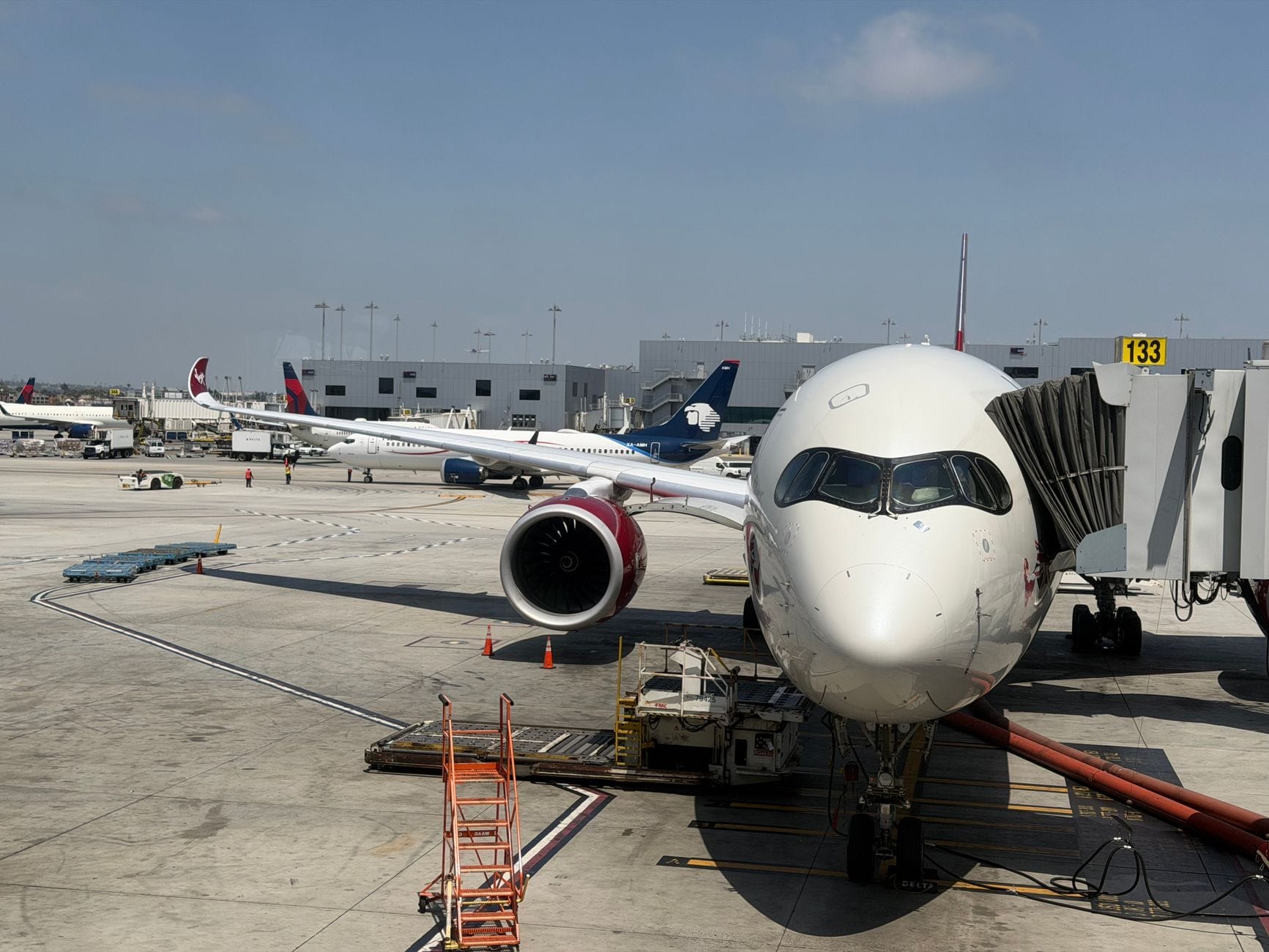 Vista ampla de um portão moderno de aeroporto com um grande avião na ponte de embarque e outros aviões ao fundo.