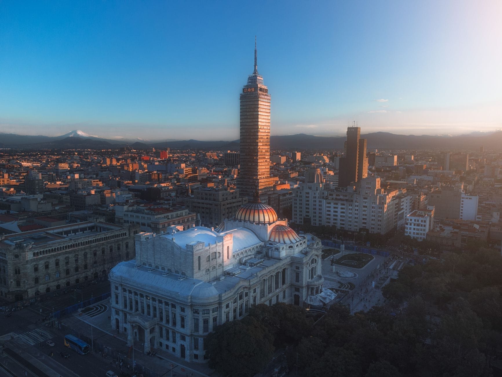 Vista aérea da Cidade do México ao pôr do sol com a Torre Latinoamericana, o Palácio de Belas Artes e as montanhas ao fundo.