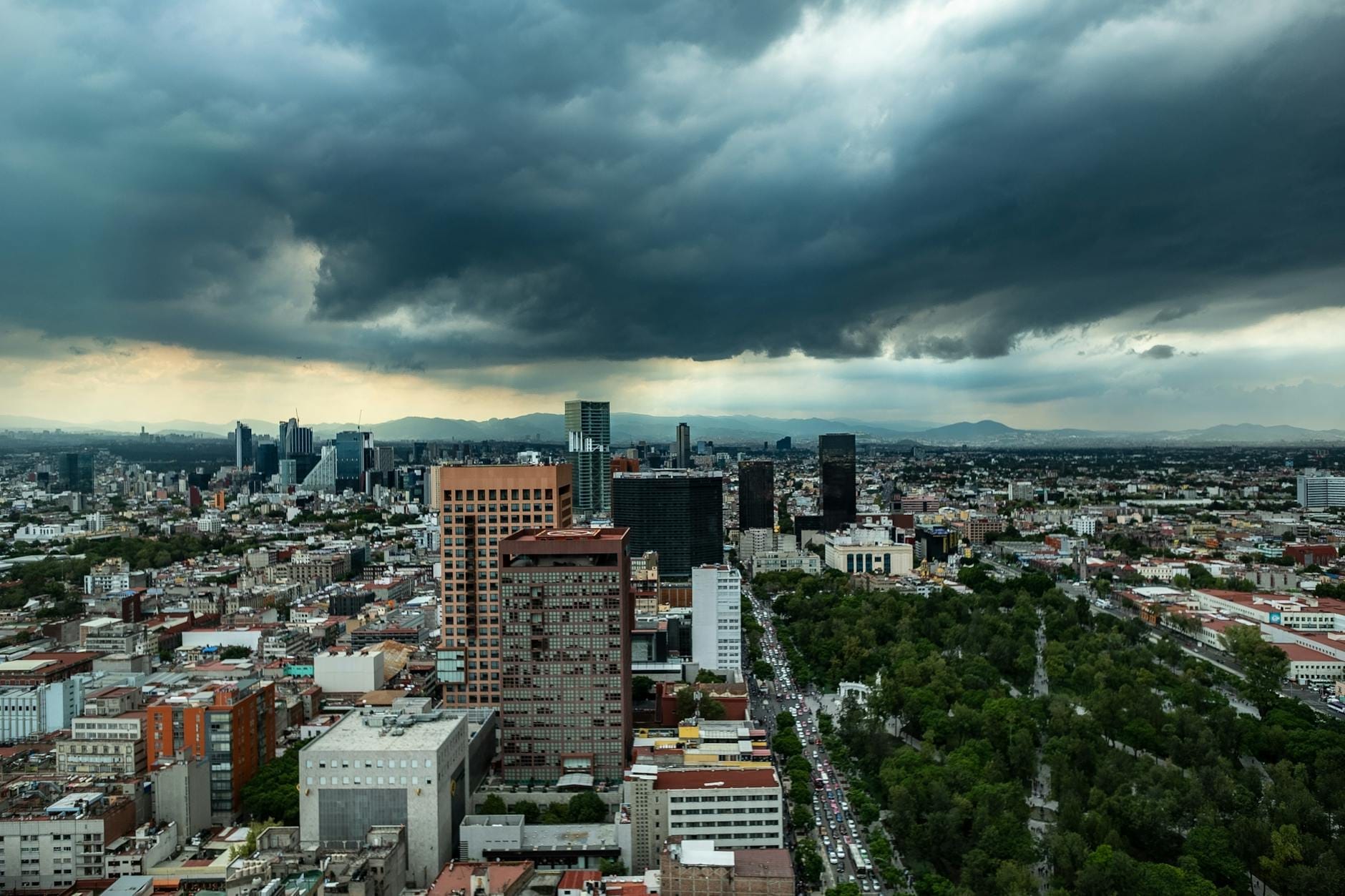 Vista ampla do horizonte de Mexico City com dramáticas nuvens da estação chuvosa e áreas verdes visíveis na paisagem urbana.
