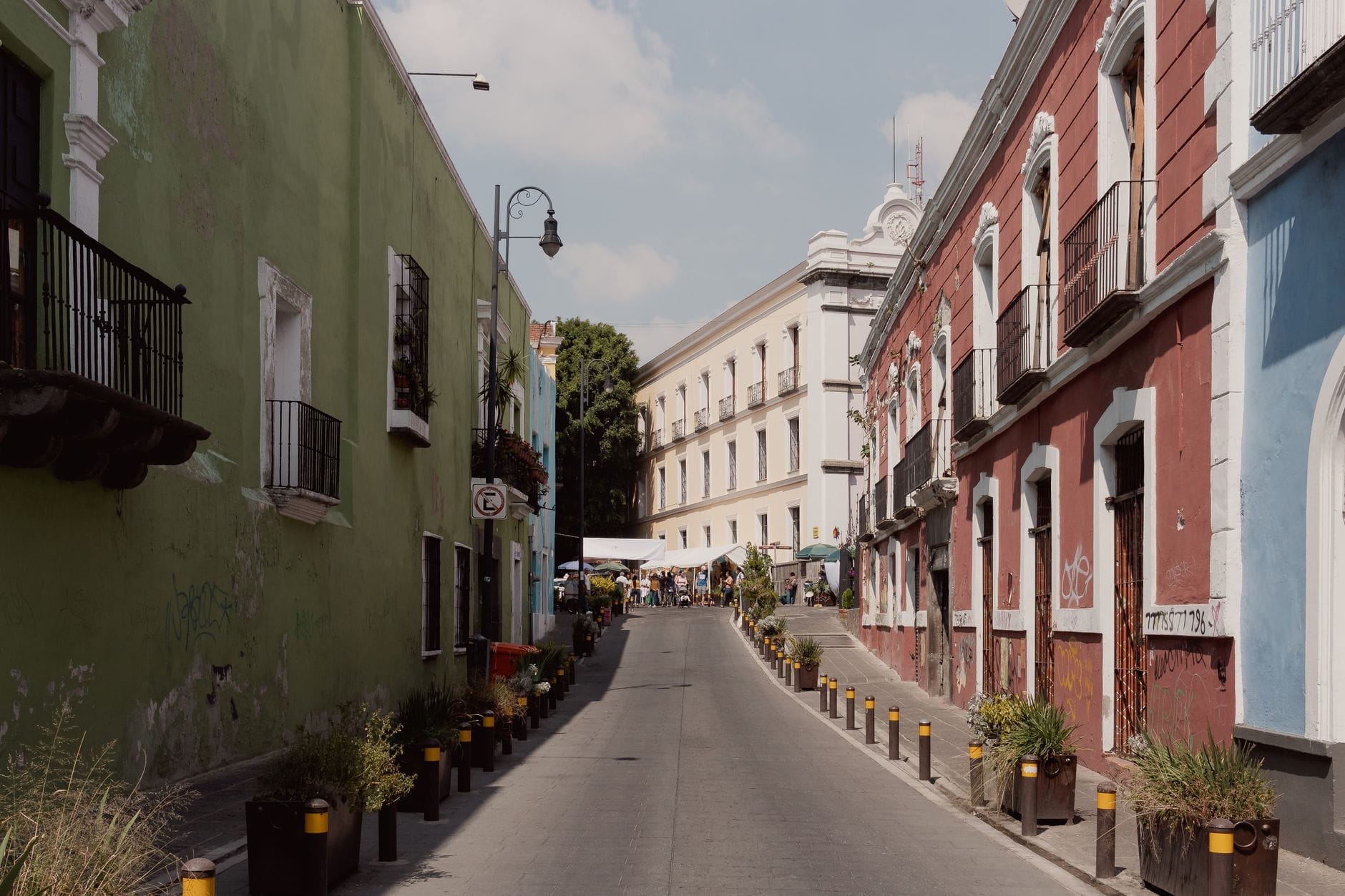 Encantadora rua estreita na Cidade do México ladeada por coloridos edifícios históricos e plantas em vasos, evocando uma atmosfera de bairro acolhedor e convidativo.