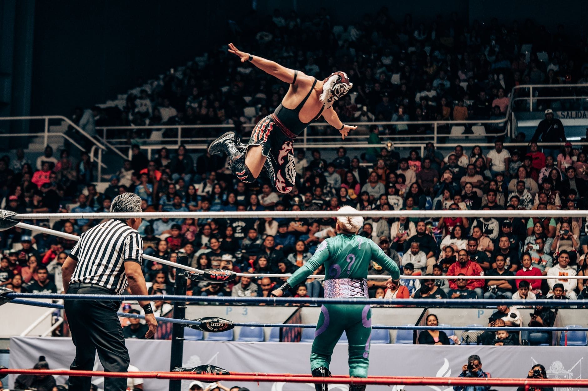 Lutadores mascarados se apresentando em uma animada luta livre diante de uma arena lotada, uma experiência local autêntica na Cidade do México.