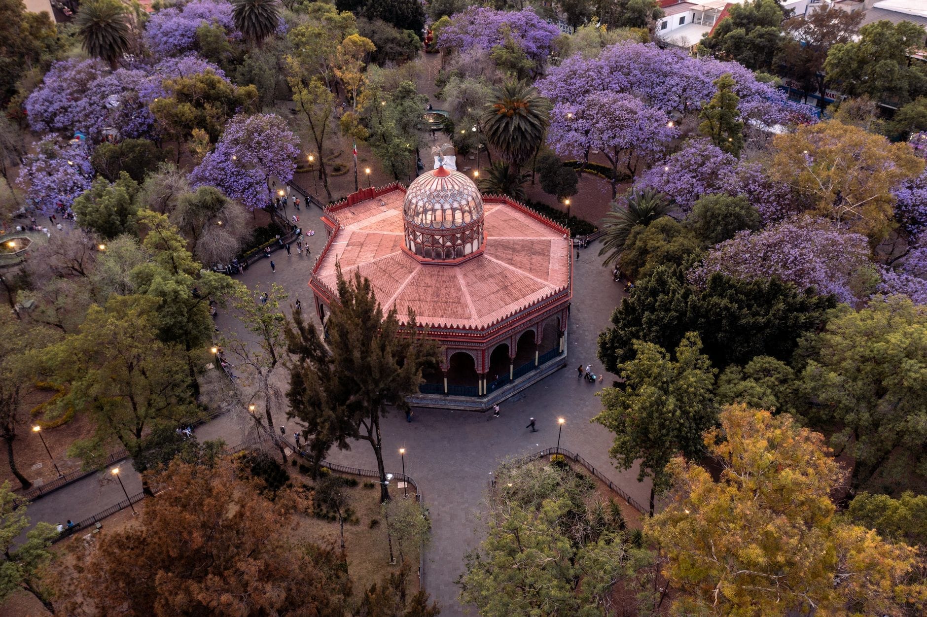Vista aérea do icônico Kiosko Morisco octogonal em Coyoacán rodeado por árvores com flores roxas de jacarandá.