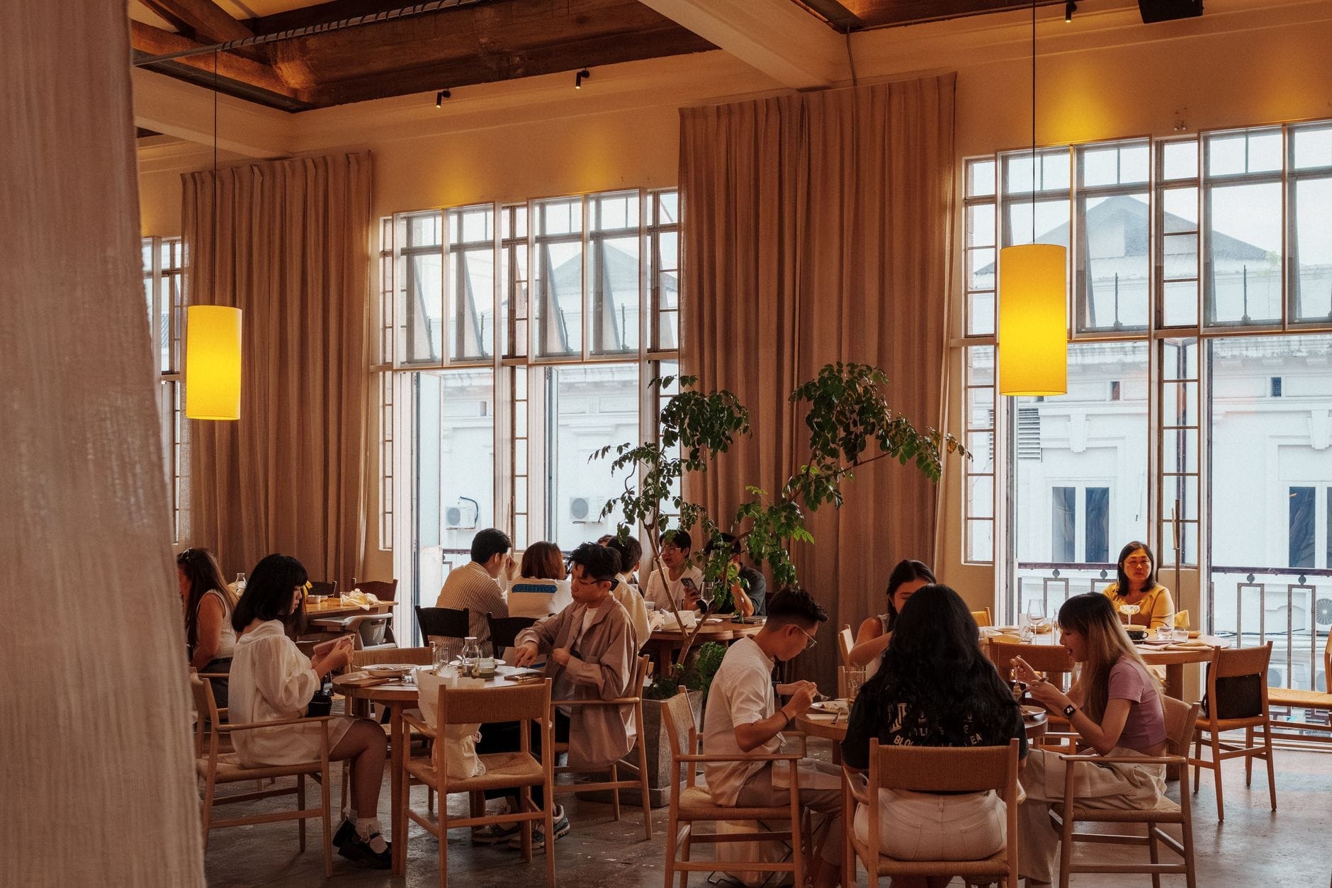 Interior de restaurante sofisticado durante o dia com grandes janelas, iluminação elegante, mobiliário moderno e clientes a desfrutar das suas refeições numa atmosfera animada.